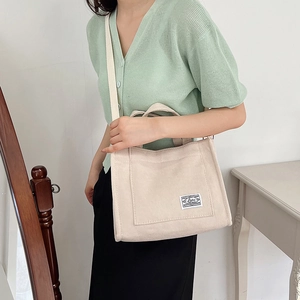 Beige corduroy tote bag with dual straps and woven label shown in a lifestyle setting