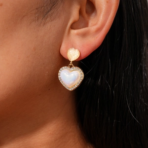 Detail of a gold heart-shaped earring with opal-like stone and sparkling crystal frame