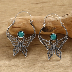 Detail of silver hollow butterfly earrings with turquoise stone on wooden base