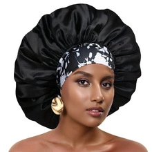 Detail of a large black satin sleep cap with a printed headband on a female model