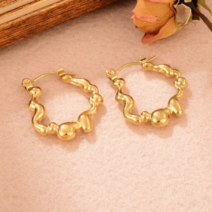 Détail de boucles d'oreilles créoles dorées ondulées sur fond minimaliste texturé