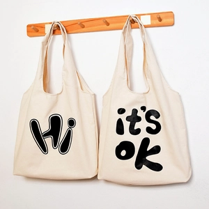 Detailed view of casual beige canvas tote bags featuring stylish 'Hi' and 'it's ok' prints.