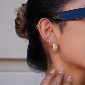 Close-up of irregular 14K gold C-shaped earrings with pleated texture and pavé accents