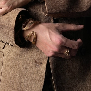 Detail of gold twisted spiral metal bracelets and ring on brown herringbone suit sleeve