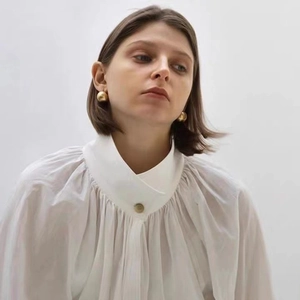 Élégantes boucles d'oreilles boules dorées et chemise à col montant sur mannequin femme