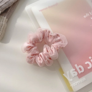 Pink sheer mesh hair scrunchie with daisy print on a notebook background