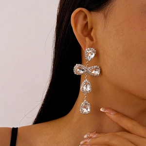 Close-up of silver drop earrings with rhinestones and bow detail worn by a model