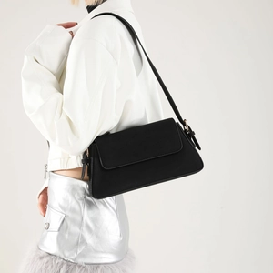Side view of matte black baguette bag with adjustable strap worn by fashion model