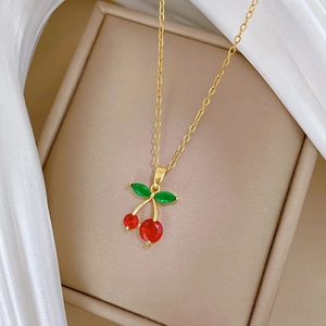 Elegant gold titanium necklace with sparkling red cherry pendant on white satin background