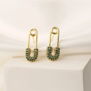 Close-up of gold safety pin earrings with green crystals on a white display stand