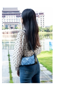 Blue denim shoulder bag with quilted stitching and black leather strap worn by a model