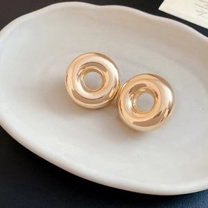 Close-up of golden C-shaped hoop earrings with a polished mirror finish on a ceramic plate