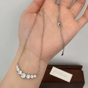 Elegant silver smile necklace featuring seven cubic zirconia stones on a wooden jewelry box