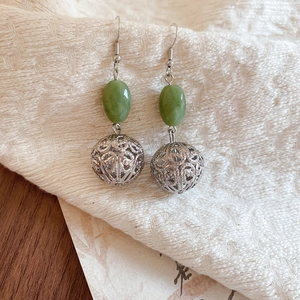 Détail de boucles d'oreilles argentées en résine avec perle verte dans un style rétro