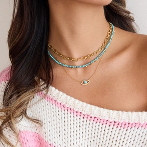 Layered gold necklace featuring turquoise beads and a sparkling evil eye pendant on model