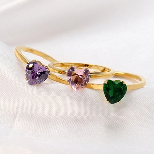 Three 18K gold heart-shaped gemstone rings in purple, pink and green on white silk