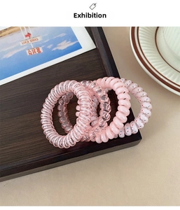 Set of four pink spiral hair ties with polka dots on a wooden tray detail view
