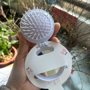 Detail of white foldable hairbrush with integrated mirror and pink bow pattern