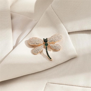 Elegant gold dragonfly brooch with green gems and white rhinestones on beige suit