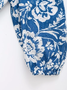 Dettaglio di ricamo inglese floreale blu su un top slim con scollo a V e polsini elastici