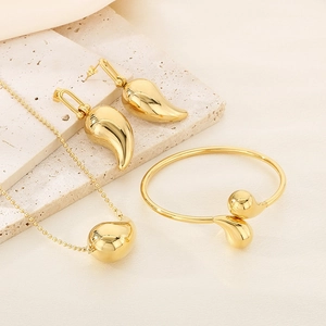 Detail of polished gold jewelry set featuring teardrop earrings and sleek ball cuff