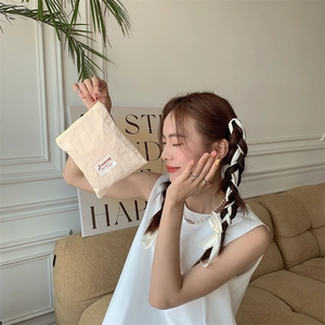 Close-up of a small beige fabric cosmetic bag held by a model in a cozy home setting