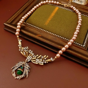 Gros plan du pendentif feuille en bronze avec gemme verte sur collier de perles roses