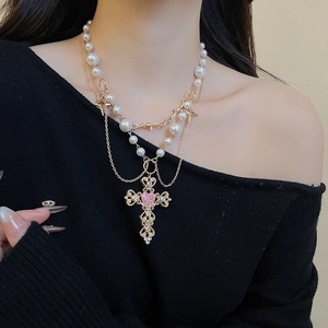 Detail of layered pearl necklace featuring gold cross pendant with pink heart gemstone