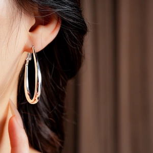 Close-up of a model wearing a large silver geometric U-shaped hoop earring with polished finish