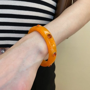 Detail of orange acrylic bangle with gold-set rhinestones and white sand texture