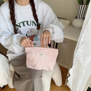 Pink corduroy makeup bag with top zipper and woven label detail held by model