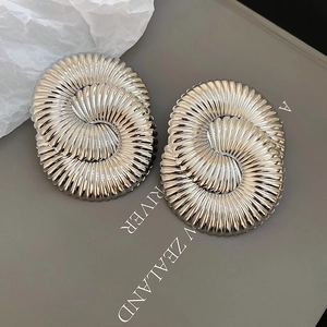 Macro detail of silver geometric spiral earrings with textured metallic finish on gray magazine