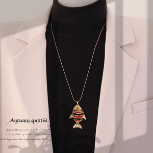 Detail view of a vintage gold koi fish pendant necklace worn by a model over a black turtleneck