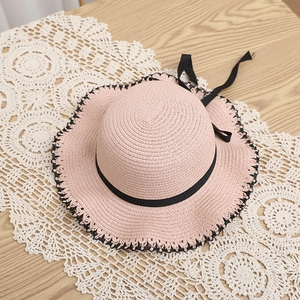 Detail of pink straw hat featuring black lace trim and a satin bow on a wooden table