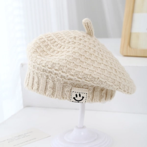 Dettaglio del berretto in maglia beige con patch smiley e trama di lana spessa