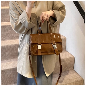 Detail of brown glossy oil wax leather satchel bag featuring silver square buckles and strap