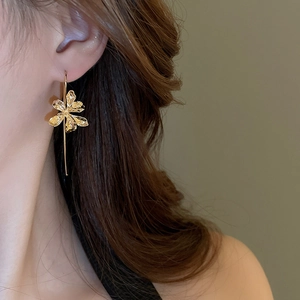 Macro detail of textured golden lily flower earring with elegant long drop pendant