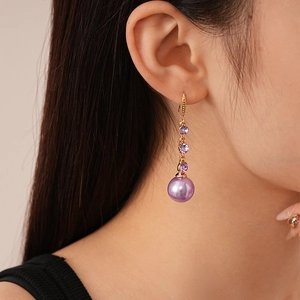 Detail of drop earrings with purple faux pearls and round crystals in golden finish
