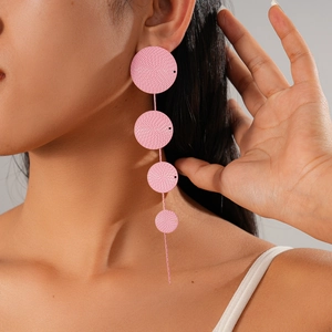 Detailed close-up of pink layered circular tassel earrings on a model with weave texture