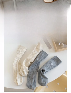 Détail de chaussettes en maille torsadée avec broderie lettre S en crème et gris
