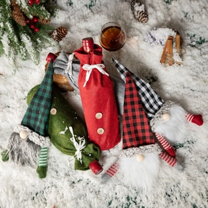 Festive Christmas gnome wine bottle covers in checkered patterns on snowy background