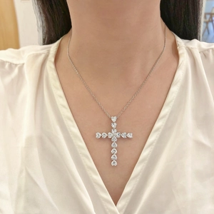 Macro view of a silver cross pendant with heart-shaped zircon stones on a model