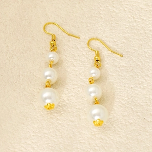 Detail view of triple pearl drop earrings with gold floral caps and hook findings