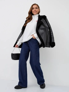 Full-body shot of a black faux shearling jacket, white sweatshirt, and wide-leg jeans outfit