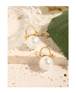 Close-up of white round pearl drop earrings with gold hooks on a textured stone base