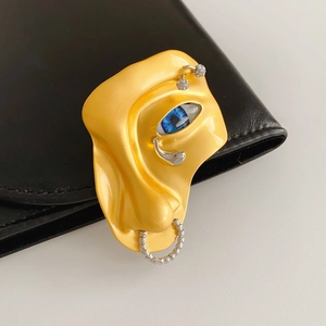 Macro detail of surrealist face brooch with a realistic blue eye and silver nose ring