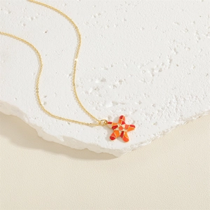 Close-up of a gold starfish necklace with red-orange gradient enamel on a stone pedestal