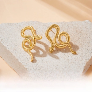 Macro detail of gold-plated snake earrings with scale textures on stone background