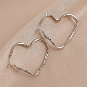Détail de créoles en forme de cœur argenté avec design ondulé sur soie rose