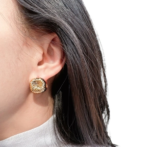 Close-up of golden round stud earrings with sunburst texture on a female model